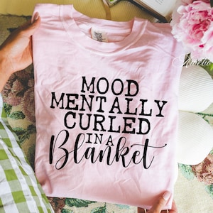 Puede incluir: Camiseta rosa con texto negro que dice "Mood Mentally Curled In A Blanket".