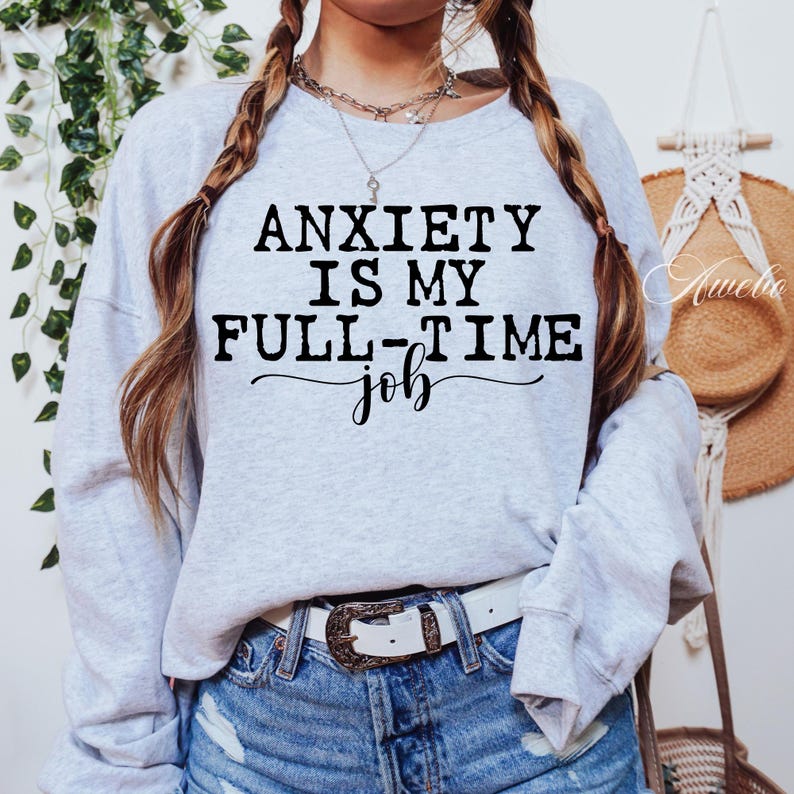 Puede incluir: Sudadera gris con el texto "La ansiedad es mi trabajo de tiempo completo" en letras negras.