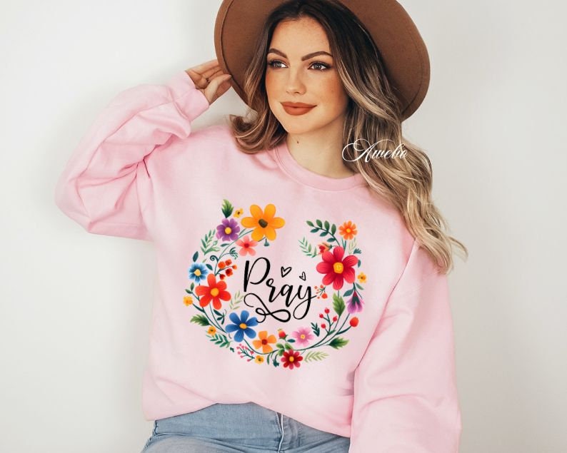 May include: Pink sweatshirt with a floral wreath design and the word "Pray" in black lettering.