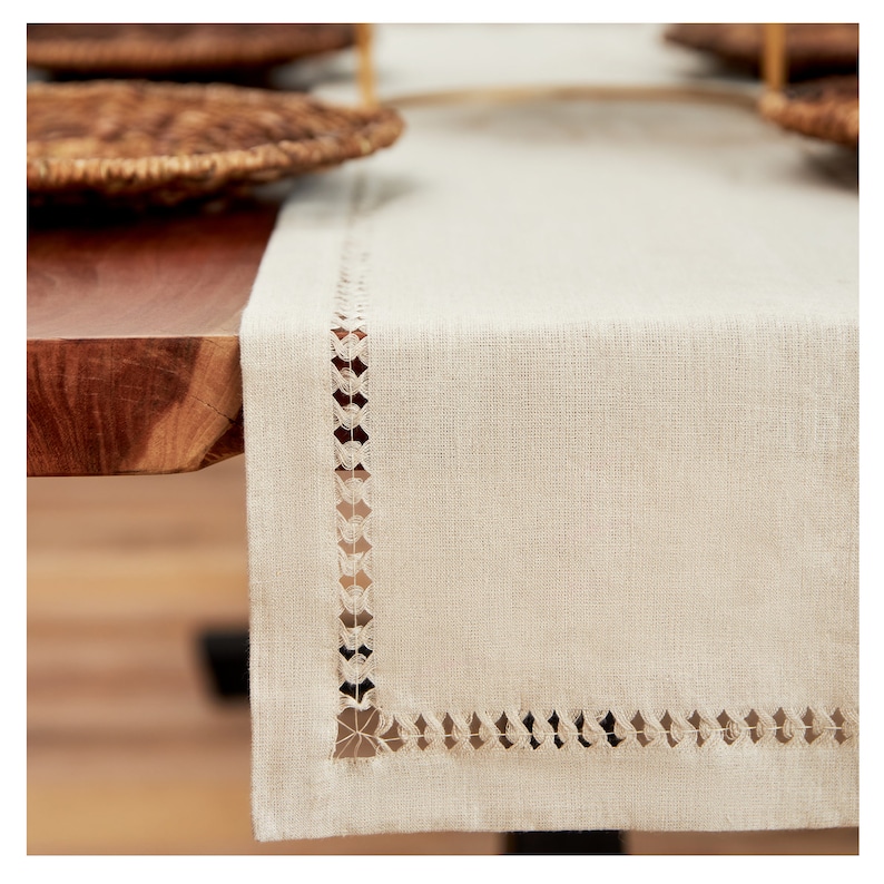 May include: A beige linen table runner with a delicate white lace trim. The runner is on a wooden table.