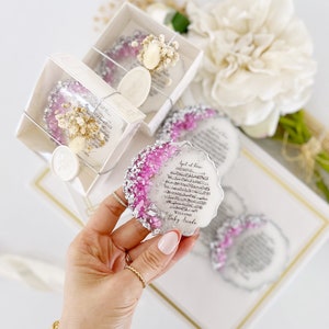 May include: A white and silver round resin keepsake with pink glitter and Arabic calligraphy. The text reads "Surah al-Kafirun" and "Welcome Baby Arida".