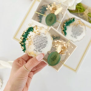 May include: A white, round, resin coaster with gold leaf and green accents. The coaster features Arabic calligraphy and a green wax seal with a leaf design. The text reads "Ayat al-Kursi" and "Welcome Baby Malik".