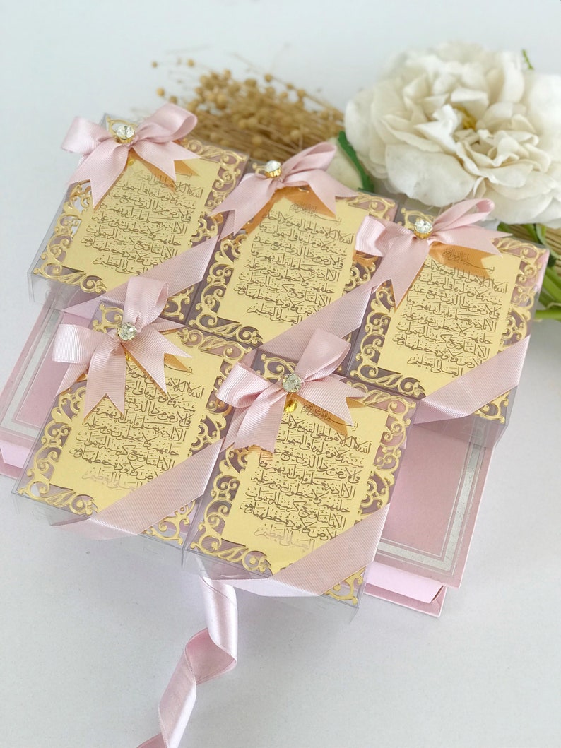 May include: Five small pink gift boxes with gold-colored decorative trim and a gold-colored inscription in Arabic. Each box is tied with a pink ribbon and a small rhinestone.
