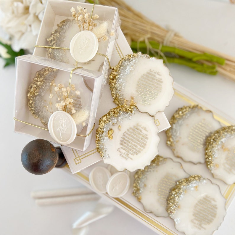 May include: Set of six white coasters with gold glitter and a gold rim. Each coaster has a white wax seal with a leaf design. The coasters are packaged in white boxes with gold trim.