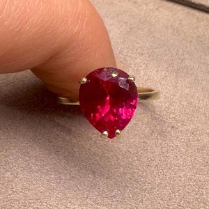 Può includere: Un anello con un rubino a forma di pera incastonato in oro giallo. Il rubino è di colore rosso intenso e ha una taglio sfaccettato.