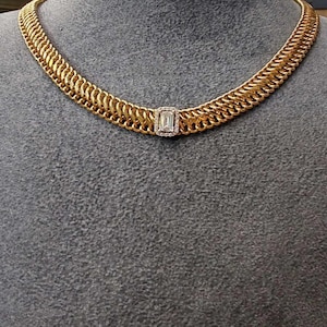 May include: A gold chain necklace with a large, rectangular, clear gemstone in the center. The chain is made of interlocking links.