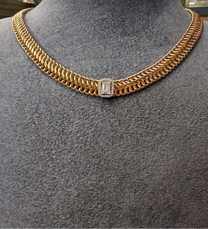 May include: A gold chain necklace with a large, rectangular, clear gemstone in the center. The chain is made of interlocking links.