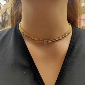 May include: A gold chain choker necklace with a small square-shaped diamond pendant.