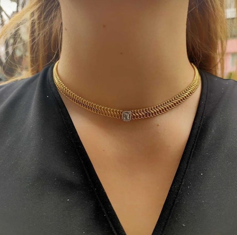 May include: A gold chain choker necklace with a small square-shaped diamond pendant.