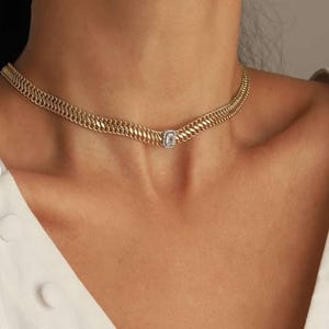 May include: A gold chain choker necklace with a single square-shaped clear stone pendant.