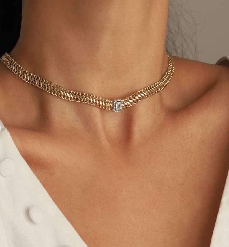 May include: A gold chain choker necklace with a single square-shaped clear stone pendant.