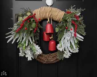 May include: A Christmas wreath with a rope base, red berries, and frosted pine branches. Three red bells hang from the wreath.