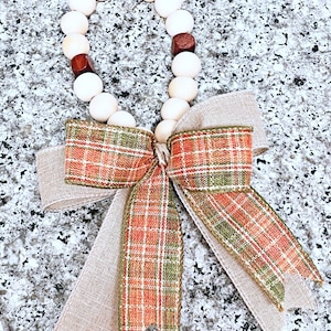 May include: A wooden bead garland with a plaid and burlap bow. The garland is made of natural wood beads and has a rustic, farmhouse style.
