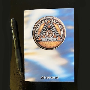 May include: A small, brown, metal coin with a triangle design and the words "To Thine Own Self Be True" around the outside. The triangle has the words "Unity", "Service", and "Recovery" on each side. The center of the triangle has the Roman numeral "IV" and the date "07-19-2016".