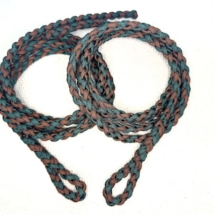 May include: A braided rope made of two colors, brown and green. The rope is looped and tied at the ends, creating a decorative knot.