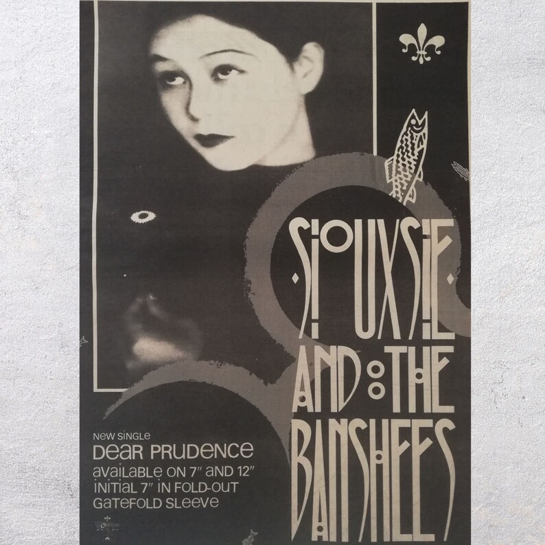May include: Black and white promotional poster for the band Siouxsie and the Banshees. The poster features a black and white photo of Siouxsie Sioux, the band's lead singer, and the band's name in a stylized font. The text "NEW SINGLE DEAR PRUDENCE AVAILABLE ON 7" AND 12" INITIAL 7" IN FOLD-OUT GATEFOLD SLEEVE" is printed at the bottom of the poster.