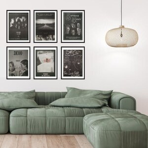 May include: A living room interior with a green sectional sofa and a matching ottoman. Six black framed posters are hung on the wall above the sofa. The posters feature black and white images of bands and music groups, including Devo, Soft Cell, and Depeche Mode.