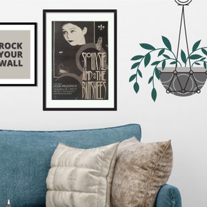 May include: A black and white poster with a photo of Siouxsie Sioux, the lead singer of the band Siouxsie and the Banshees. The poster is framed in black and has the band's name in large, stylized letters. The text on the poster reads "Dear Prudence" and "Available on 7" and 12" Initial 7" in fold out Gatefold Sleeve."