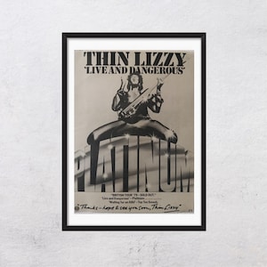 May include: Black and white framed poster featuring Thin Lizzy's 'Live and Dangerous' album art. The poster includes a band member playing a guitar, the word 'PLATINUM', and tour details. The poster is in a black frame.