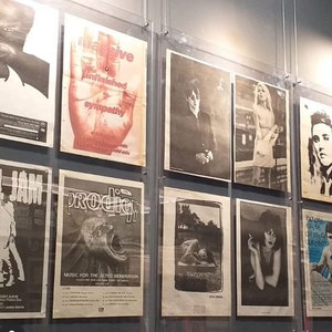 May include: A wall display of framed posters featuring various music artists and bands, including a poster with the text "Massive Unfinished Sympathy" and a poster with the text "Prodigy Music for the Jilted Generation".