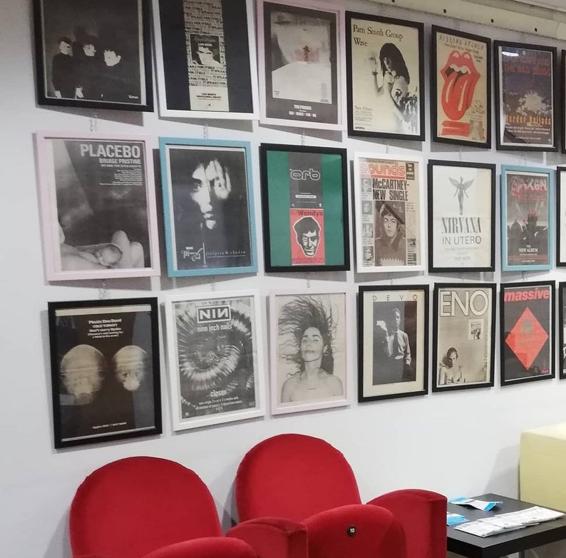 Puede incluir: Una pared con una colecci&oacute;n de p&oacute;sters de m&uacute;sica enmarcados que presentan bandas como Placebo, Nirvana y NIN. Los p&oacute;sters son de varios colores y estilos, y algunos incluyen t&iacute;tulos de &aacute;lbumes y logotipos de bandas.