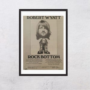 May include: A framed poster featuring a black and white graphic of Robert Wyatt with a large head on a small body. The text reads ROBERT WYATT and ROCK BOTTOM, accompanied by printed reviews from New Musical Express and Melody Maker magazines.