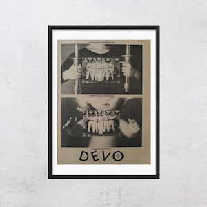 May include: Black framed poster featuring a vintage advertisement for the band Devo. The poster has two panels with images of a person holding a metal object and a baby. The band's name is printed in large letters at the bottom.