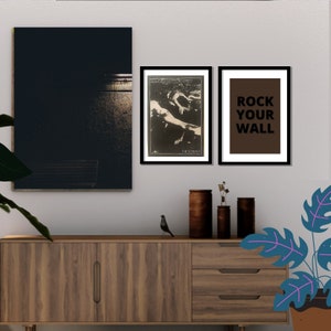 May include: Two framed posters on a white wall above a wooden dresser. The poster on the left is black and white and features a photo of a band called "Sound and the Fury" with the text "The Scream". The poster on the right is brown with white text that says "Rock Your Wall".