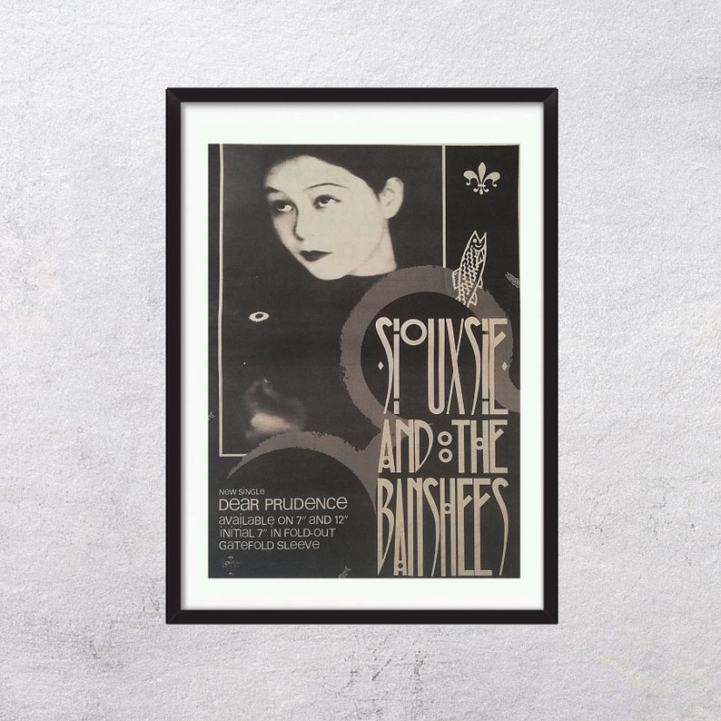May include: Black and white promotional poster for the band Siouxsie and the Banshees. The poster features a black and white photo of Siouxsie Sioux, the band's lead singer, and the band's name in a stylized font. The text "NOW SINGLE DEAR PRUDENCE AVAILABLE ON 7" AND 12" INITIAL 7" IN FOLD-OUT GATEFOLD SLEEVE" is printed at the bottom of the poster.