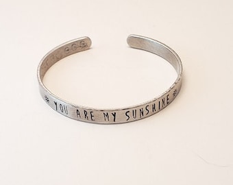 May include: A silver bracelet with the inscription "You are my sunshine" engraved on it.
