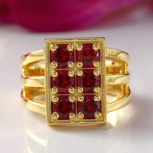 Peut inclure: Une bague en or avec un plateau rectangulaire serti de six pierres précieuses rondes rouge foncé disposées en deux colonnes verticales. L'anneau se compose de trois bandes dorées parallèles qui se rejoignent sur les côtés pour soutenir le chaton.