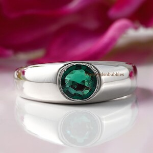 Puede incluir: Un anillo de plata con una piedra preciosa verde redonda engastada.