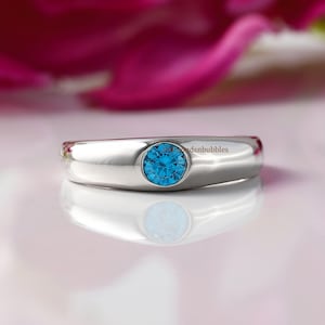 Puede incluir: Un anillo de plata con una piedra preciosa azul engastada en el centro. El anillo es simple y elegante.