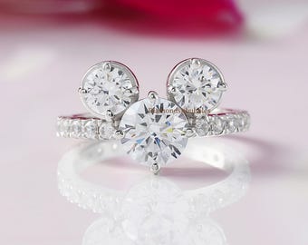 May include: A silver ring with three round clear stones set in a Mickey Mouse shape. The ring is set with smaller clear stones around the band.