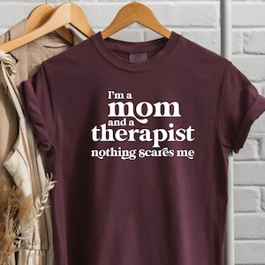 Puede incluir: Camiseta color burdeos con texto blanco que dice "Soy una mamá y una terapeuta, nada me asusta"