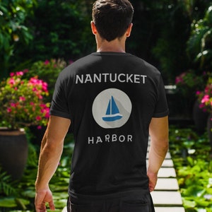 Könnte beinhalten: Ein schwarzes T-Shirt mit weißem Text, der "NANTUCKET HARBOR" lautet, und einem weißen Kreis mit einem blauen Segelboot darin.