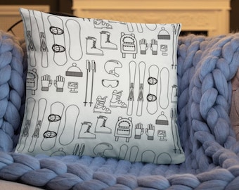 May include: A white throw pillow with a black and white pattern of winter sports equipment, including skis, snowboards, boots, gloves, and hats.