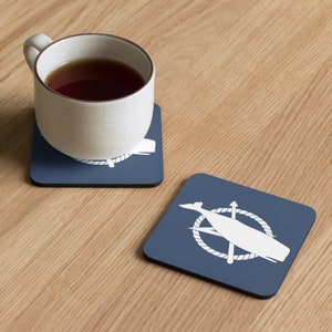 May include: Two blue square coasters with a white whale and harpoon design. The whale is inside a rope circle with a harpoon crossing through it.