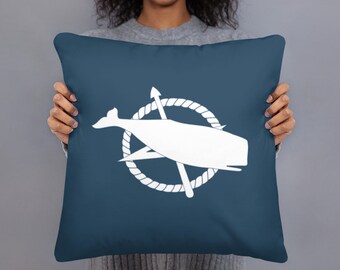 May include: A blue throw pillow with a white whale and compass design. The whale is inside a rope circle with a compass needle and arrow.