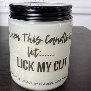 May include: A white candle with a black lid and the text "When this candle is lit.....LICK MY CLIT" and "Handmade in Canada by Flameboyant Candle".