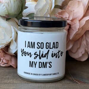 May include: A white candle with a black lid and a label that reads "I AM SO GLAD you slid into MY DM'S". The label also includes the text "HANDMADE IN CANADA BY FLAMEBOYANT CANDLE CO.".