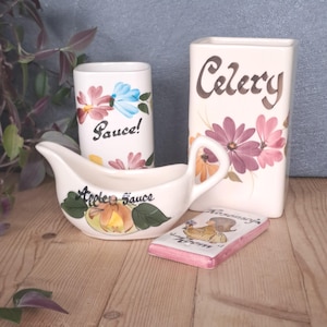 May include: A collection of vintage ceramic kitchenware. Includes a gravy boat with "Apple Sauce" text, a rectangular container labeled "Celery", a small cup with "Sauce!" text, and a small rectangular dish with "Rosemary" text.