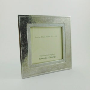 May include: A square pewter photo frame, measuring 8.9 x 8.9 cm, with a textured border and a smaller, dotted inner frame. The text "Pewter Photo Frame 3.5 x 3.5" is visible. The frame is labeled "hand made in England" by Lancaster & Gibbings.