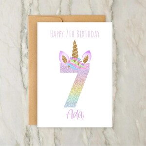 Puede incluir: Una tarjeta blanca con un n&uacute;mero 7 de purpurina arco&iacute;ris con una cabeza de unicornio en la parte superior. La tarjeta dice "Feliz 7&ordm; cumplea&ntilde;os Ada".