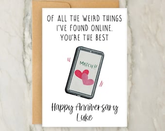 May include: A white card with a black and white illustration of a smartphone with two red hearts on the screen. The text on the card reads "Of all the weird things I've found online. You're the best. Match!! Happy Anniversary Luke."