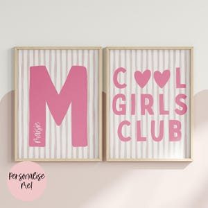 May include: Two framed wall art prints with a light pink and white vertical striped background. The left print features a large pink letter M with the name Maisie written vertically. The right print displays the pink text COOL GIRLS CLUB with two pink hearts.