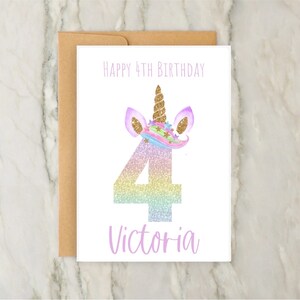 May include: A birthday card with a unicorn design. The card features a pastel rainbow number 4 with glitter, a unicorn horn, and the text "Happy 4th Birthday" and "Victoria". The card is paired with a brown envelope.