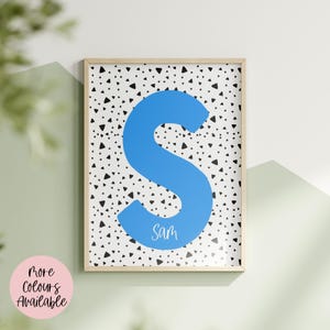 Può includere: Stampa artistica incorniciata con una grande lettera "S" blu brillante su sfondo bianco con forme triangolari nere. Il nome "Sam" è scritto in corsivo in basso sulla lettera. La cornice è di colore legno chiaro.