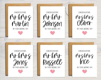 May include: Six white wedding greeting cards with brown envelopes. Each card features the text CONGRATULATIONS, followed by personalized names like Mr & Mrs Martin, Mr & Mr Johnson, Mrs & Mrs Oliver, Mr & Mrs Jones, Mr & Mr Russell, and Mrs & Mrs Ince, with ON YOUR WEDDING DAY and a pink heart.