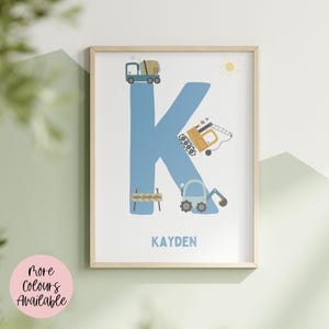 May include: A framed wall art print featuring a large blue letter K decorated with construction vehicle illustrations including a cement mixer, an excavator, and a crane. The text "UNDER CONSTRUCTION" appears on a small sign, and the name "KAYDEN" is printed below in blue.